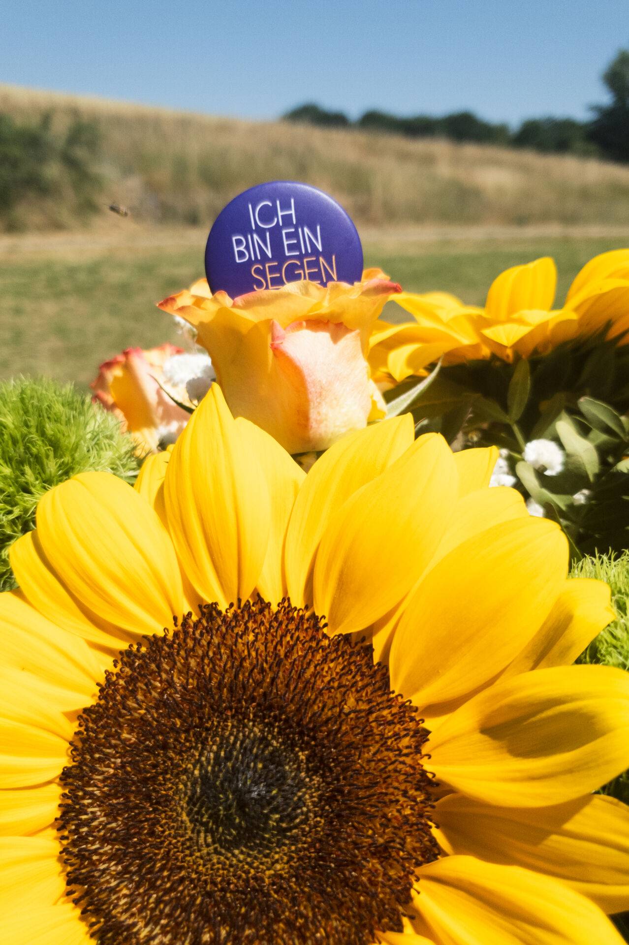 Blumenstrauß mit dem Motto des Tauffestes auf einem Ansteckbutton, der in dem Blumenstrauß steckt
